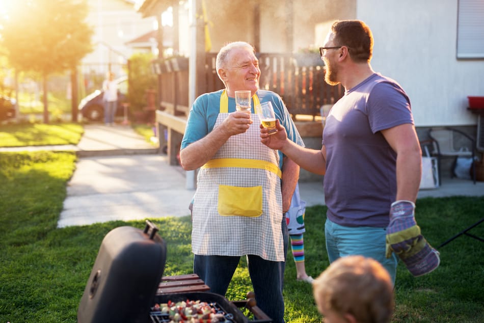 picture of Elderly Father and mature son are saluting with the beer in front of the grill in their Rhode Island house backyard on a beautiful day.