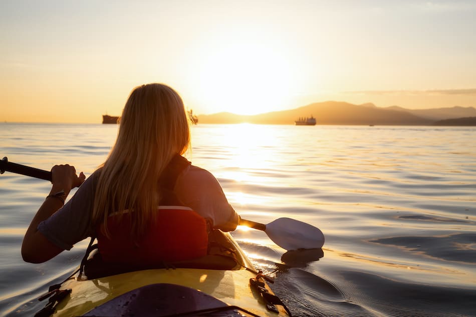 picture of Woman on a kayak is paddeling in the ocean during a vibrant sunset.